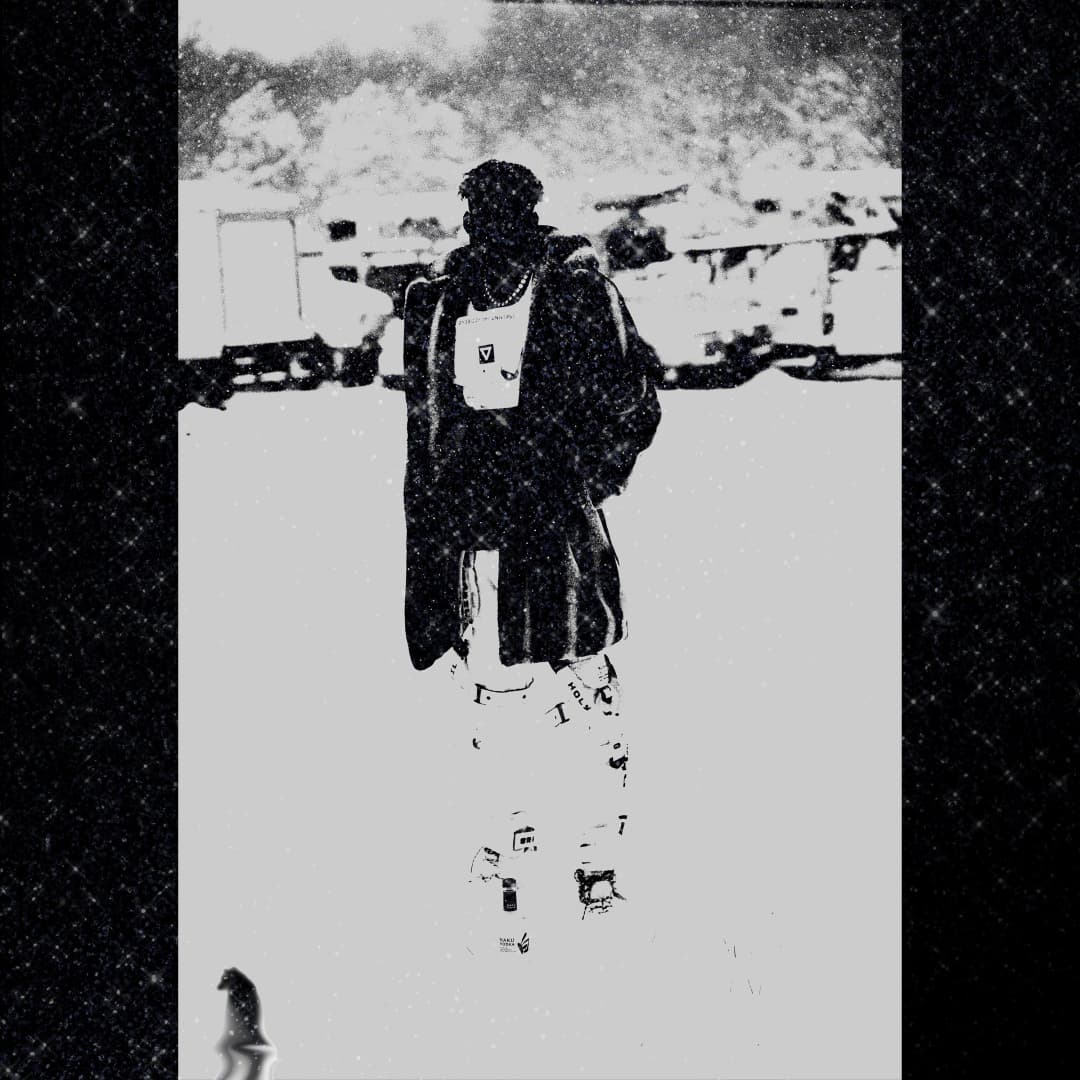 Alpha The Wolf standing with back to camera in a blizzard, wearing a long coat and chain, shot in high-contrast black-and-white with a sparkling dark border