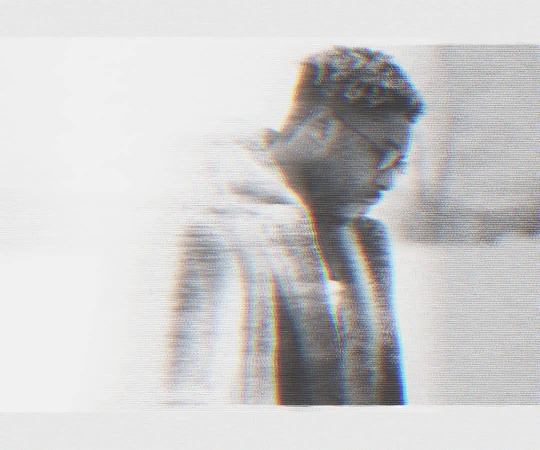 Alpha The Wolf in side profile, head bowed, wearing glasses, sharper chromatic fringing and brighter contrast — image feeling bleached and ghosted