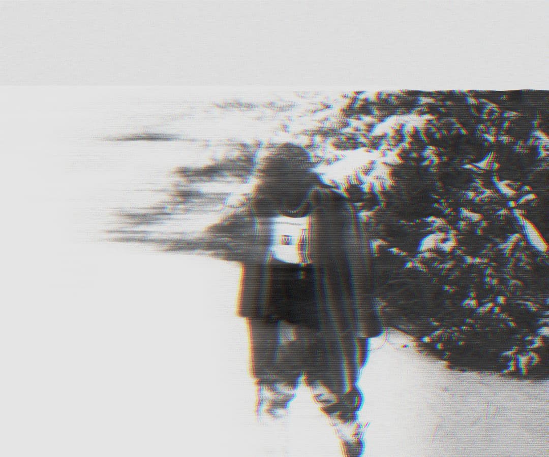 Alpha The Wolf walking through snow beside a snow-covered bush, the figure dissolving leftward in a strong horizontal motion-smear glitch