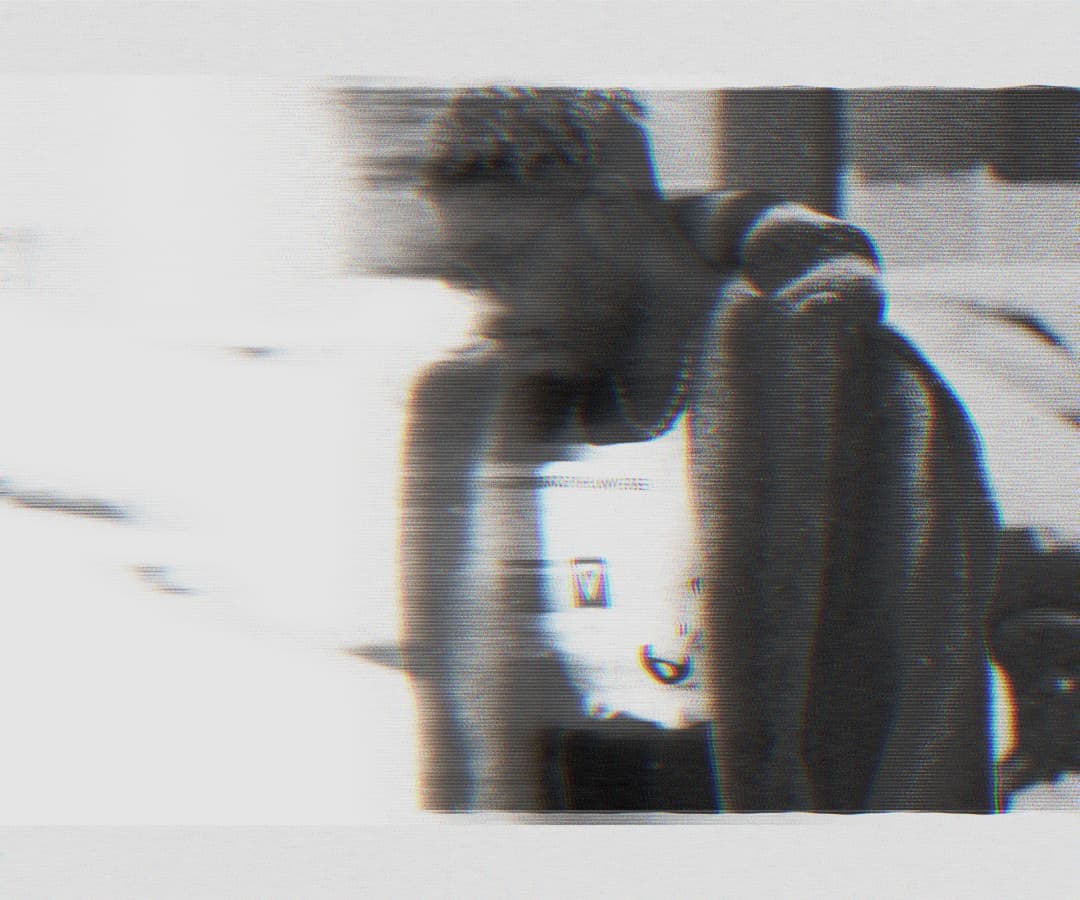 Alpha The Wolf seated, leaning forward with elbows on knees, head down, shirtless, rendered in grainy halftone with scan-line distortion and chromatic fringing