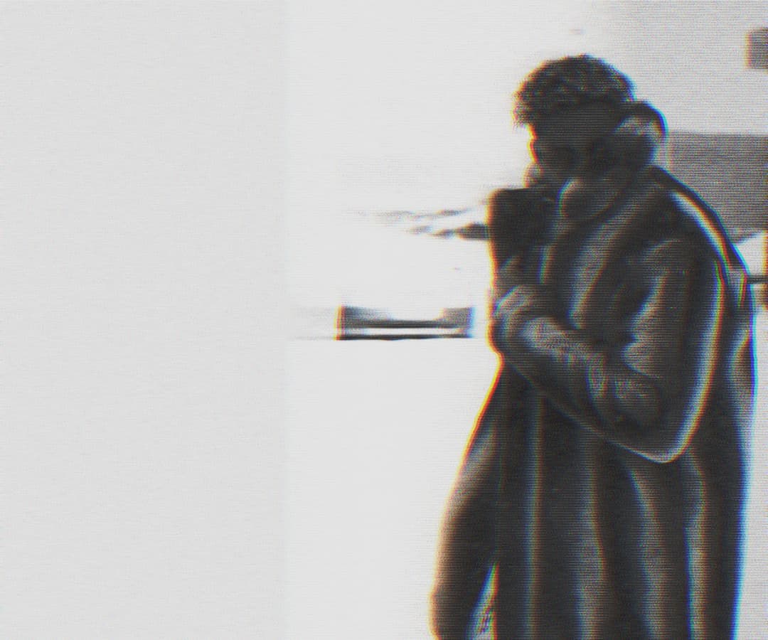 Alpha The Wolf cradling a camera close to the face, more tightly cropped than the previous frame with slightly more contrast in the glitch fringing