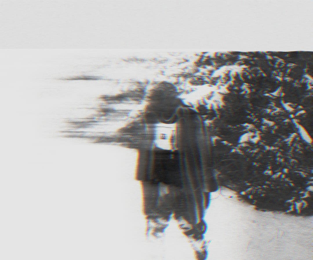 Alpha The Wolf walking through snow beside a snow-covered bush, the figure dissolving leftward in a strong horizontal motion-smear glitch