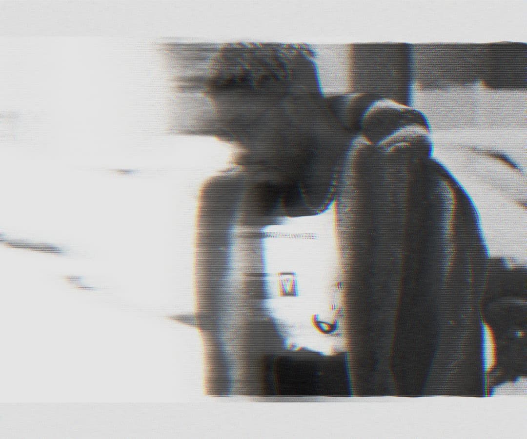 Alpha The Wolf seated, leaning forward with elbows on knees, head down, shirtless, rendered in grainy halftone with scan-line distortion and chromatic fringing
