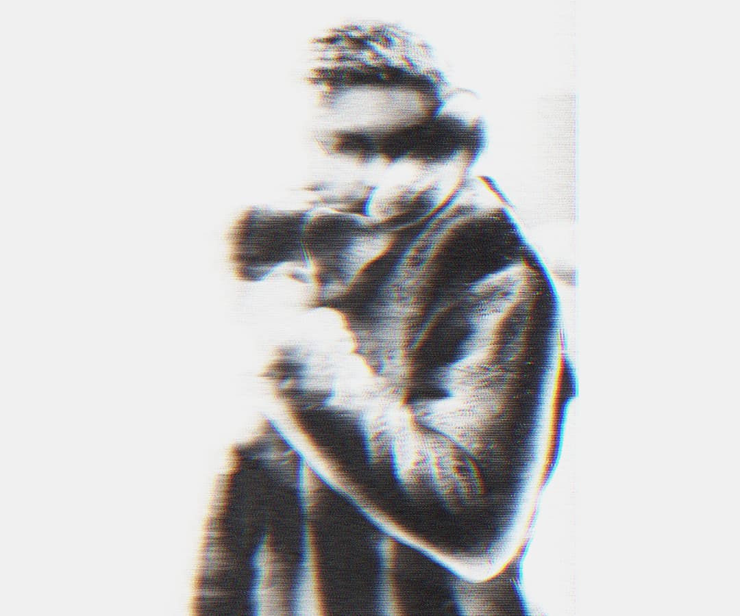 Alpha The Wolf raising a camera to the face in a close-up, the figure centered and bold, with high-contrast grain and chromatic aberration on a pale background